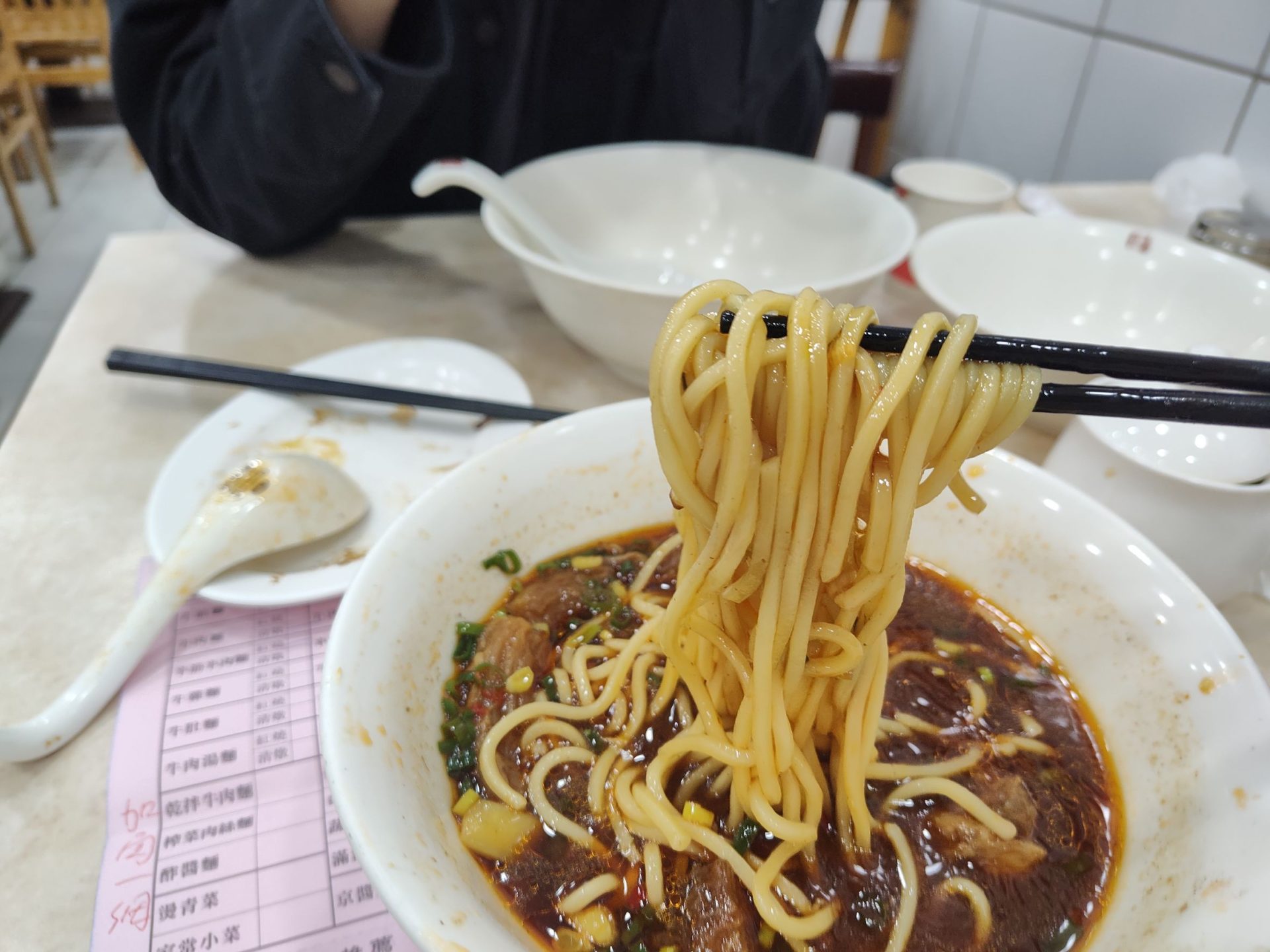 穆記牛肉麵招牌紅燒牛肉麵，筷子挑起Q彈麵條，湯頭色澤深紅濃郁，信義區必吃美食