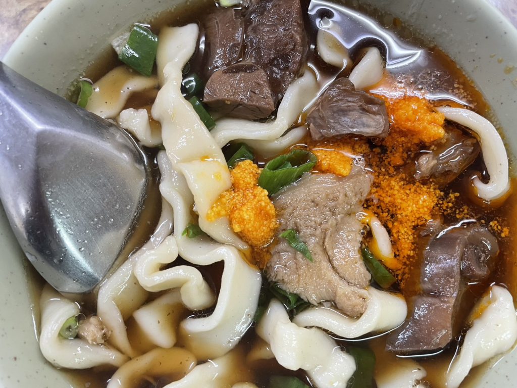 富宏牛肉麵招牌牛肉麵特寫，淋上辣油並帶筋燉煎軟嫩的牛肉塊